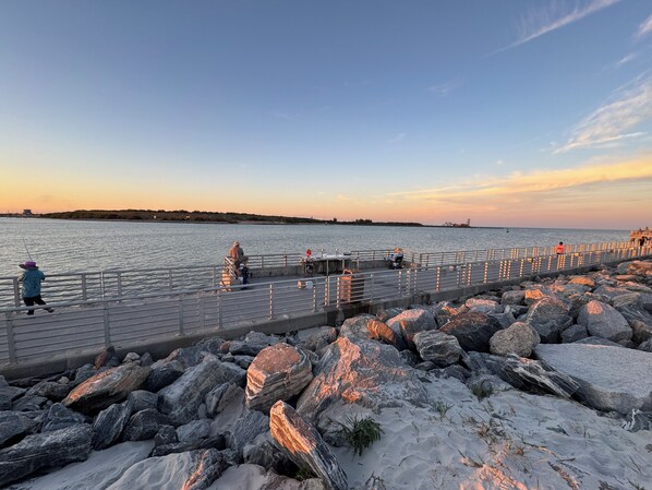 A pier with a railing, rocky shoreline, and a calm body of water.