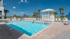 A swimming pool with lounge chairs and a covered seating area, surrounded by palm trees and a clear blue sky.
