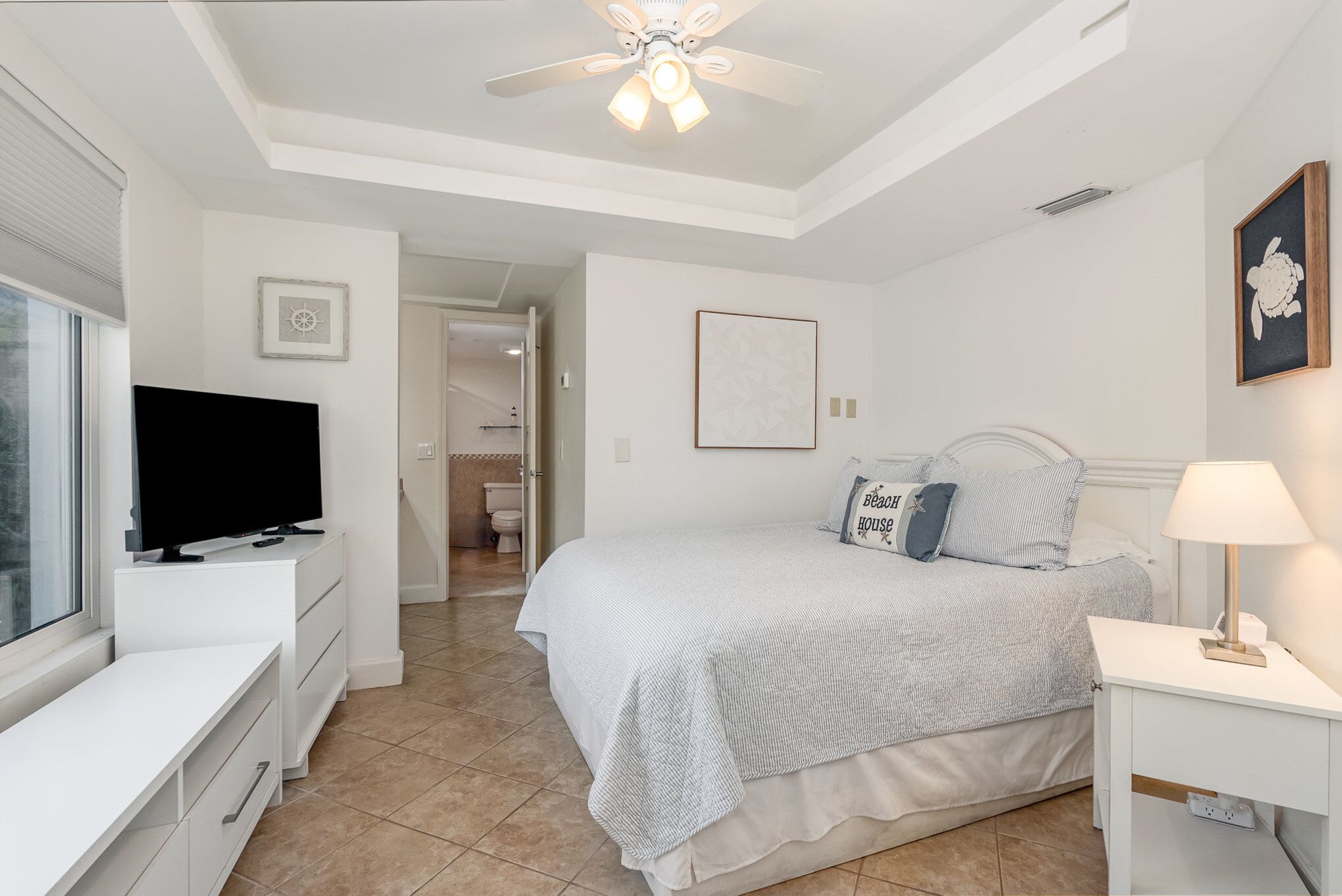 A bedroom with a bed, a TV, a desk, and a ceiling fan.