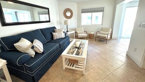 A living room with a dark blue sofa, two white armchairs, a coffee table, and a ceiling fan.