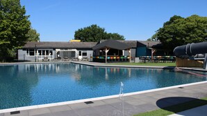 A swimming pool with a pavilion, a covered seating area, and a building with a sign that reads "Supermarket." - Chalet Retreat in Green Setting (Lathum)