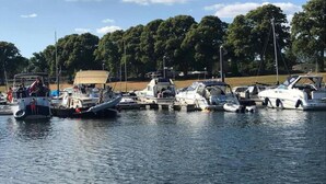 A marina with various boats docked, surrounded by trees and a clear sky. - Chalet Retreat in Green Setting (Lathum)
