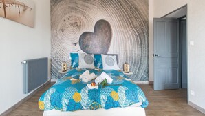 A bedroom with a large bed, a wall tapestry, and a door. - Gite in the heart of Saône et Loire (DOMPIERRE LES ORMES)