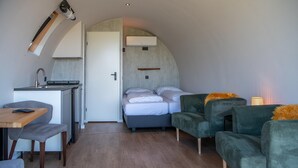 Une petite pièce comprenant un coin cuisine, un lit et deux fauteuils verts.