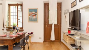 Un coin repas avec une table en bois dressée pour quatre personnes, une petite table d’appoint et un téléviseur posé sur un meuble.