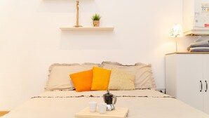Une chambre à coucher bien rangée, avec un lit, des oreillers, une table de chevet avec une lampe et une petite étagère sur laquelle est posée une plante.