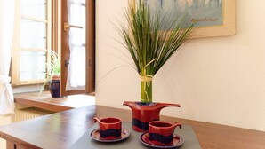 Une table à manger ornée d’une plante en pot, d’une théière rouge et de deux tasses assorties.