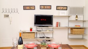 Un coin repas avec une table dressée pour deux personnes, une bouteille de vin et un téléviseur affichant le logo « NETFLIX ».