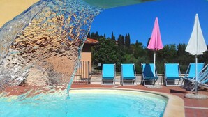 A pool with a water feature, blue lounge chairs, and umbrellas.