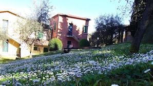 A building with a red facade, a balcony, and a garden with white flowers.
