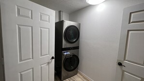 A laundry room with two stacked front-loading washing machines, a door with a handle, and a light fixture on the ceiling. - Horsing Around In the country (Dade City)