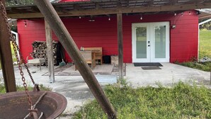 A red building with a covered porch, a door, and a small table. - Horsing Around In the country (Dade City)
