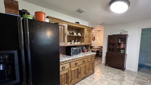 A kitchen with wooden cabinets, a black refrigerator, a microwave, and a dining area with a table and chairs. - Horsing Around In the country (Dade City)