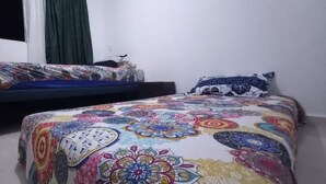 Een slaapkamer met een bed, overdekt met een kleurrijke bloemenlaken, een passend kussen en een donker hoofdbord.
