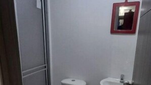 Een kleine, praktische badkamer met toilet, wastafel en spiegel.
