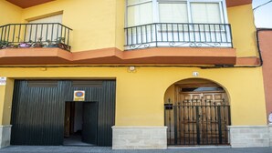 Un edificio de dos pisos con fachada amarilla, un balcón con barandilla de metal y un portón negro.