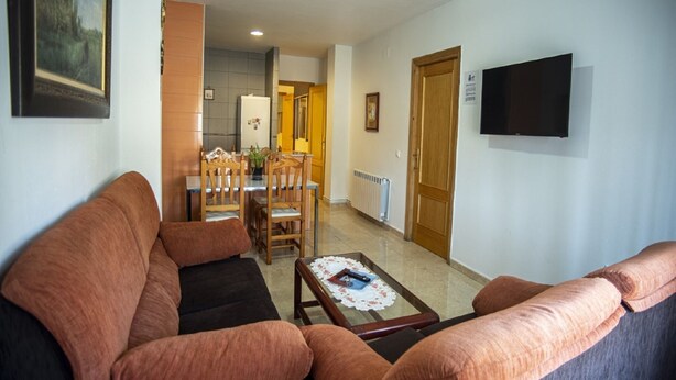 Una sala de estar con sofá, una mesa de centro, televisor y un comedor con sillas y una mesa.