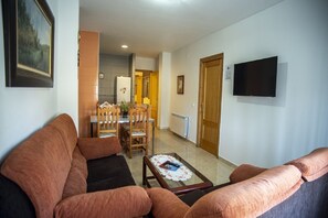 Una sala de estar con sofá, una mesa de centro, televisor y un comedor con sillas y una mesa.