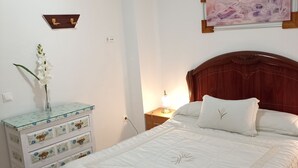 Un dormitorio ordenado con cabecera de madera, mesita de noche con lámpara y un cuadro colgado en la pared.