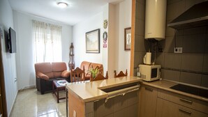 Un espacio habitable compacto con kitchenette, un sofá, una mesa de comedor y una pequeña planta.