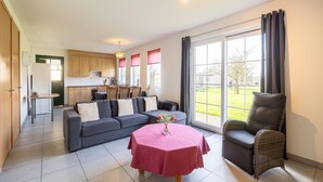 A modern living room with a sofa, a dining table with a pink tablecloth, and a wicker chair. - Eco-friendly apartment with a garden (Sint Kruis)