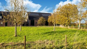 A modern building with a flat roof and solar panels, surrounded by a grassy field and trees. - Eco-friendly apartment with a garden (Sint Kruis)