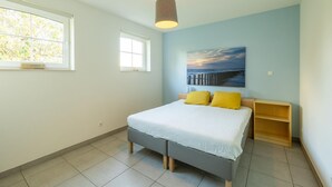 A bedroom with a bed, a bedside table, a nightstand, a window, and a painting on the wall. - Eco-friendly apartment with a garden (Sint Kruis)