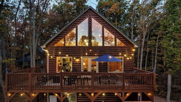 A log cabin with a balcony and deck, surrounded by trees.