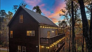 A wooden cabin with a balcony and string lights, surrounded by trees.