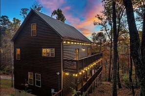 Escape to a serene forest retreat with a cozy cabin featuring a balcony and string lights.
