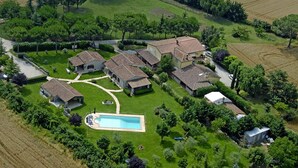 An aerial view of a residential area with multiple houses, a swimming pool, and surrounding greenery.