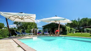 A swimming pool with lounge chairs and umbrellas, surrounded by a stone deck and greenery.