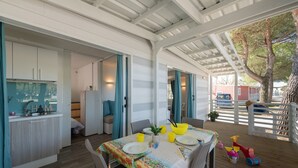A covered outdoor dining area with a table set for two, a kitchen area with cabinets and a sink, and a view of a red building in the background. - Charming Coastal Stay (Cesenatico)