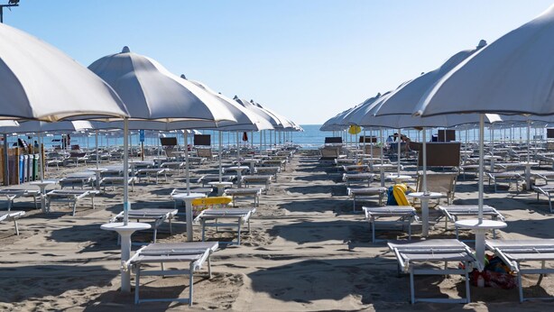 A beach with rows of white sunbeds and umbrellas, some with people, and a clear view of the sea. - Charming Coastal Stay (Cesenatico)