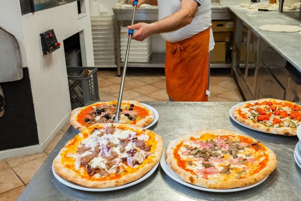 Ett kök med fyra pizzor på en arbetsbänk i rostfritt stål, en person med ett förkläde och en pizzaspade.
