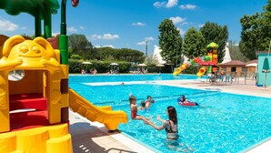 A swimming pool with a slide and play structures, surrounded by trees and umbrellas. - Charming Coastal Stay (Cesenatico)