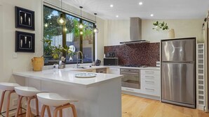 A modern kitchen with a large island, white bar stools, stainless steel appliances, and a view of greenery outside. - Elite Retreat Ponsonby with Parking and Deck (Auckland Central Suburbs)
