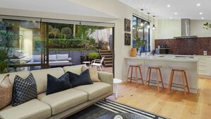 A modern kitchen with a large island, bar stools, and a dining area with a glass wall overlooking a garden. - Elite Retreat Ponsonby with Parking and Deck (Auckland Central Suburbs)