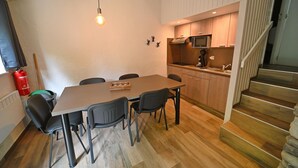 A compact kitchen with wooden cabinets, a microwave, and a sink. There is a dining table with chairs and a hanging light fixture. A fire extinguisher is mounted on the wall. - Bungalow in Virton by Vallée de Rabais Lake (VIRTON)