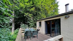 A wooden deck with a table and chairs, surrounded by lush greenery. - Bungalow in Virton by Vallée de Rabais Lake (VIRTON)