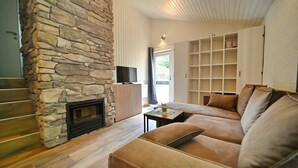 A living room with a stone fireplace, a sofa, and a television. - Bungalow in Virton by Vallée de Rabais Lake (VIRTON)