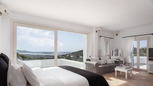 A spacious bedroom with a large bed, a sofa, and a balcony with a view of the landscape. - Villa Phos Paros (Paros)