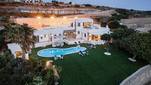 A modern villa with a swimming pool, outdoor seating, and a view of the surrounding landscape. - Villa Phos Paros (Paros)