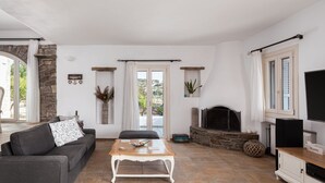A living room with a stone fireplace, a sofa, a coffee table, and a television. - Villa Phos Paros (Paros)