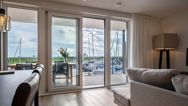 A modern hotel room with a large sliding glass door leading to a balcony with a view of sailboats.