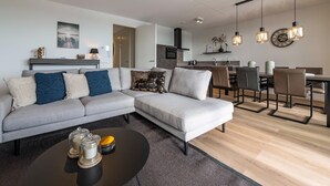 A modern living room with a grey sectional sofa, a black coffee table, and a dining area with a table and chairs.