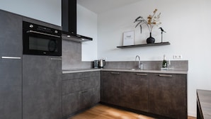 A modern kitchen with grey cabinetry, a built-in oven, a stainless steel sink, and a wooden floor.