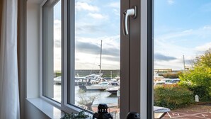 Blick auf einen Hafen mit mehreren vertäuten Booten, einem klaren Himmel und einem Ausblick auf Grün im Hintergrund.