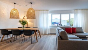 Ein modernes Wohnzimmer mit einer Couch, einem Esstisch mit Stühlen und zwei Pendelleuchten.
