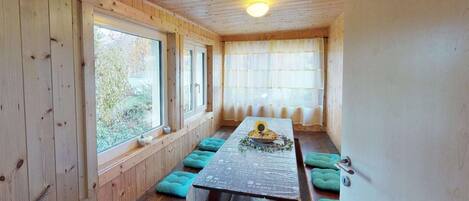 Una cabaña de madera con una larga mesa de comedor, bancos y ventanas grandes.
